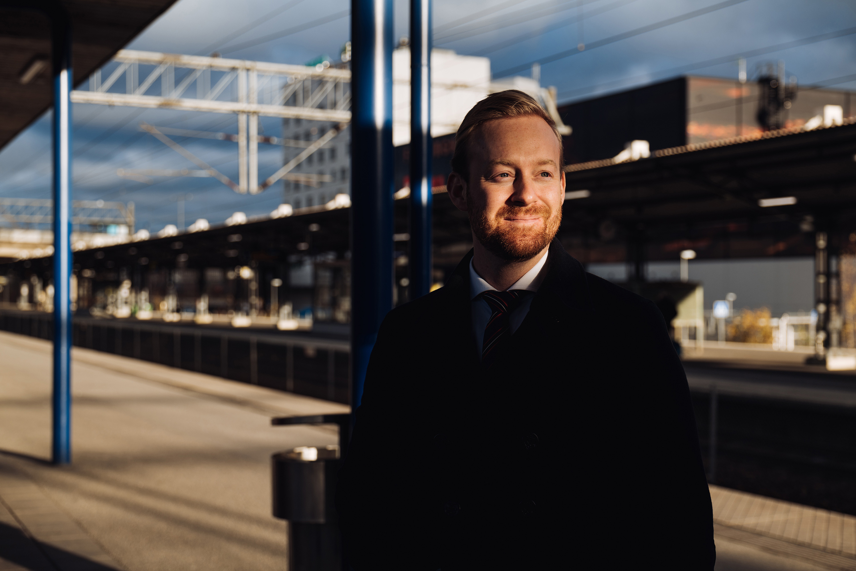 Manlig fastighetsjurist som står på solig pendeltågsperrong