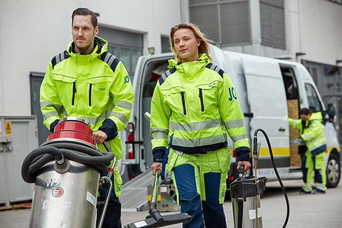 En kvinnlig och en manlig skadesanerare från Ocab gåendes från bilen med utrustning för skadesanering.