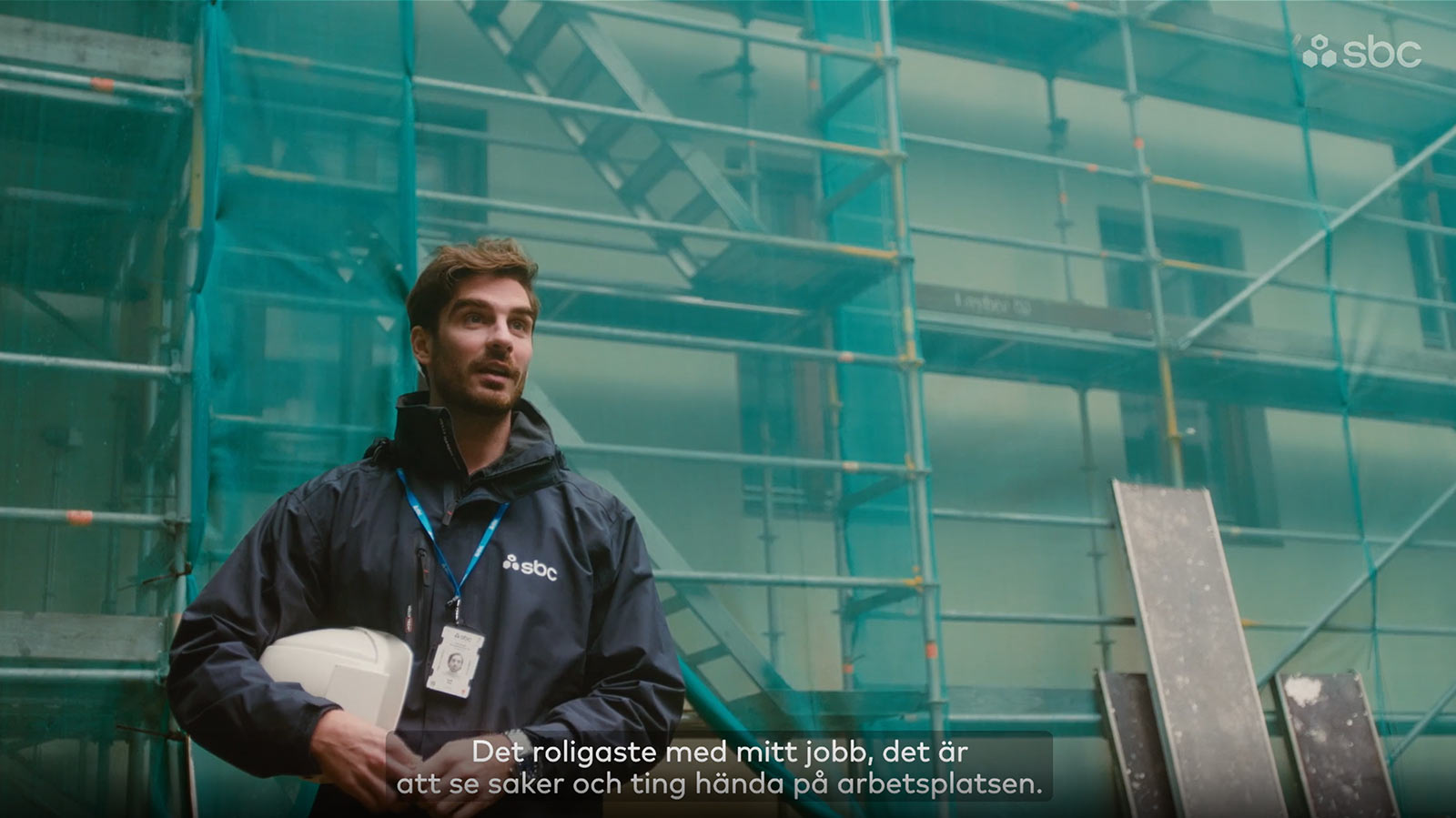 SBCs projektledare Patrik står framför en fasad med byggnadsställning och med en hjälm under armen.