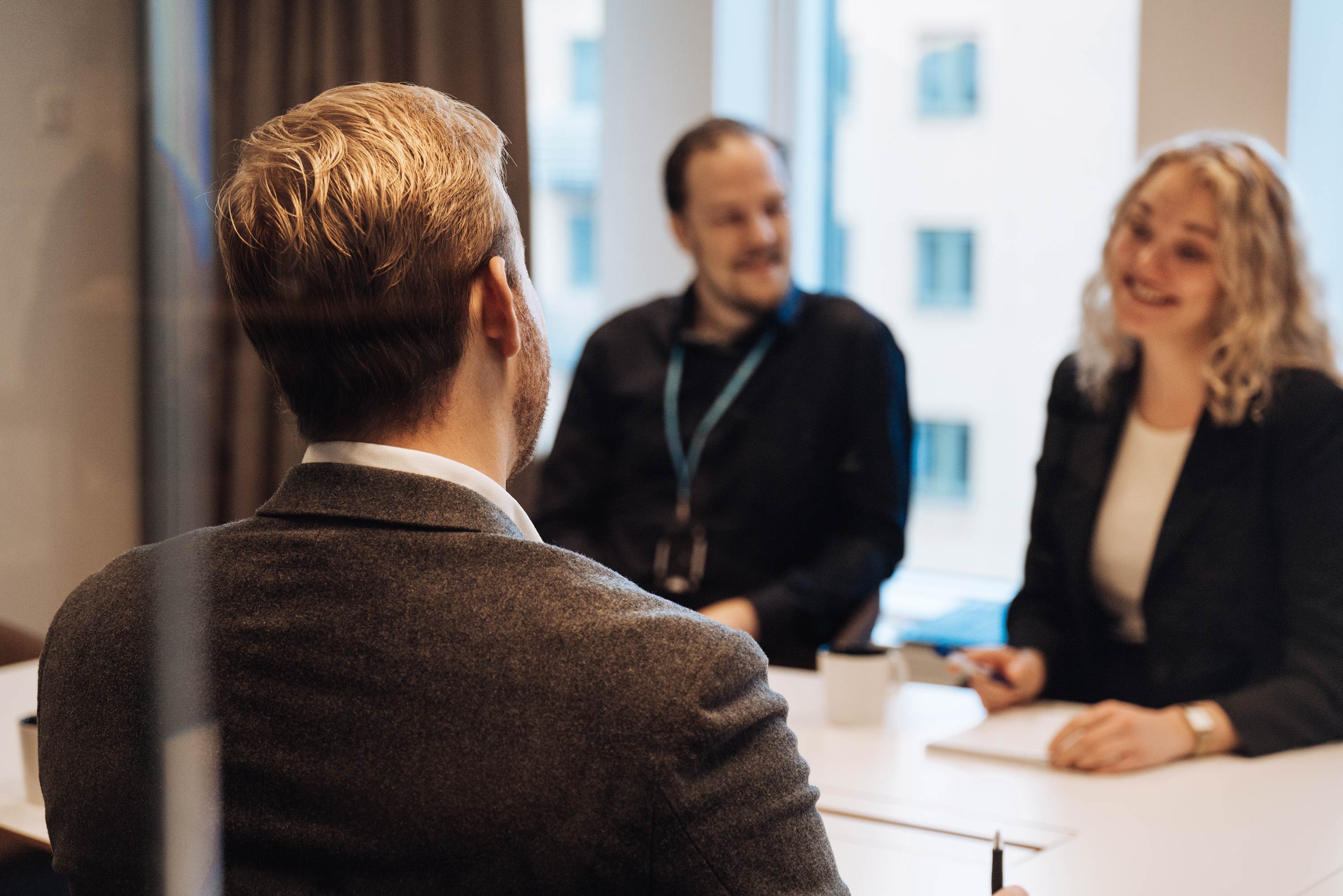 Tre personer sitter vid ett bord och pratar och ler med en kopp och anteckningsblock