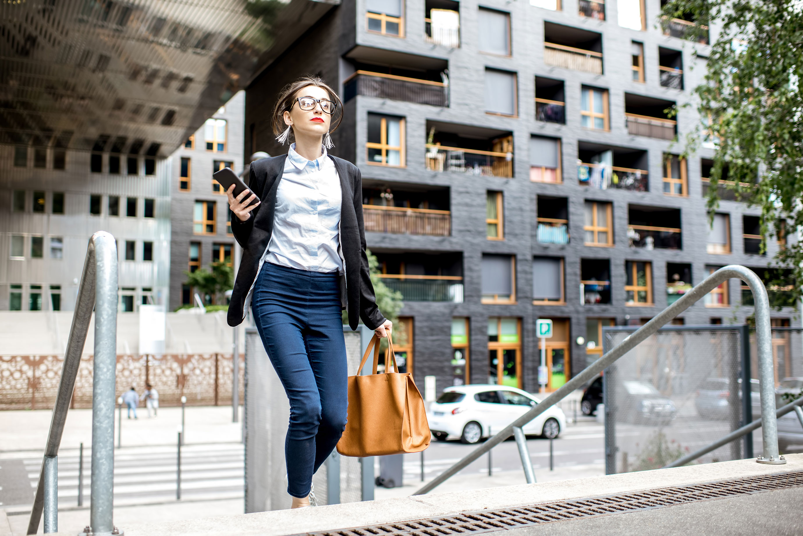 Kvinna på väg upp för trappa, håller i portfölj och mobil