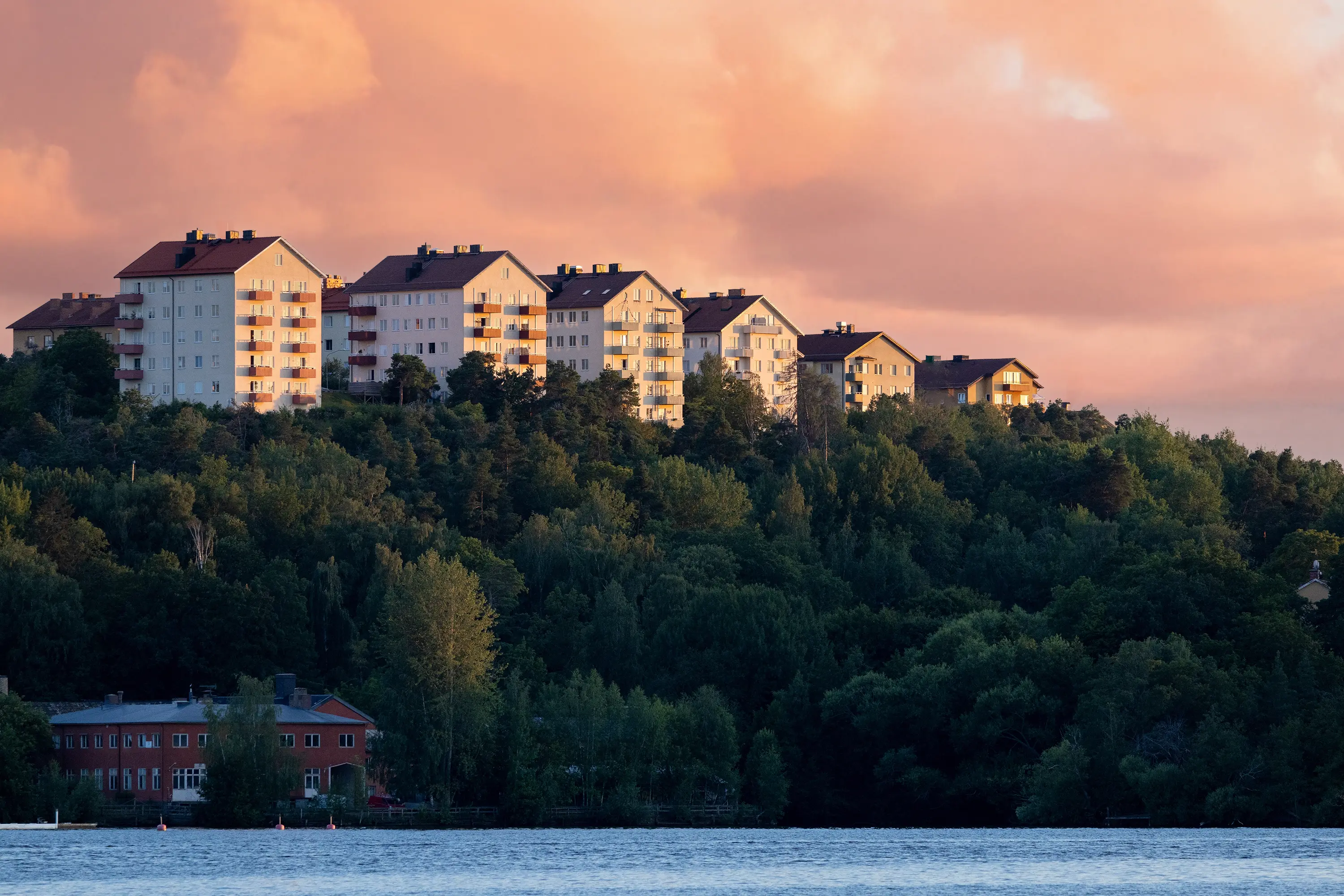 Höghus med bostadsrätter på en grön kulle vid vattnet.