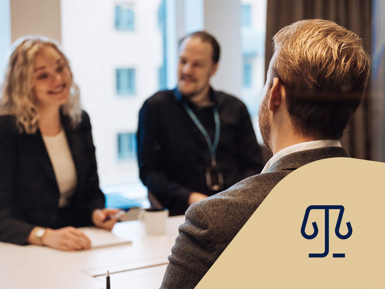 Tre jurister sitter vid ett bord och pratar och ler med ett anteckningsblock. Juridikikon.