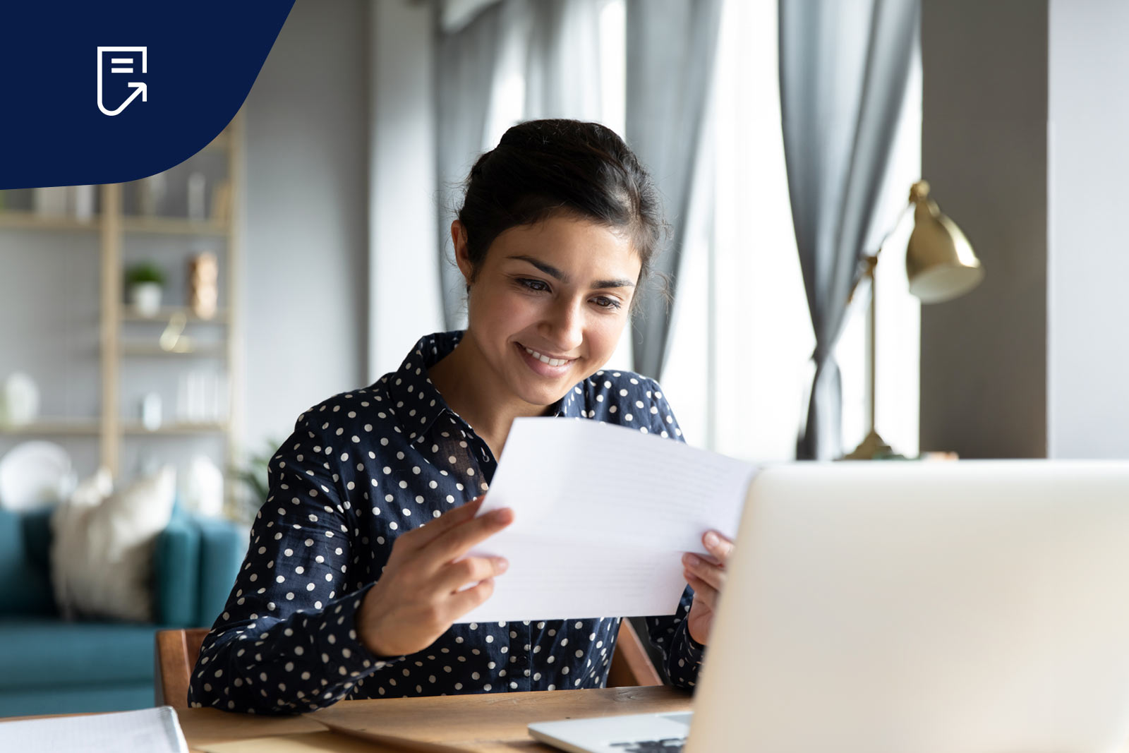 kvinna ler och läser ur ett papper med en dator framför sig