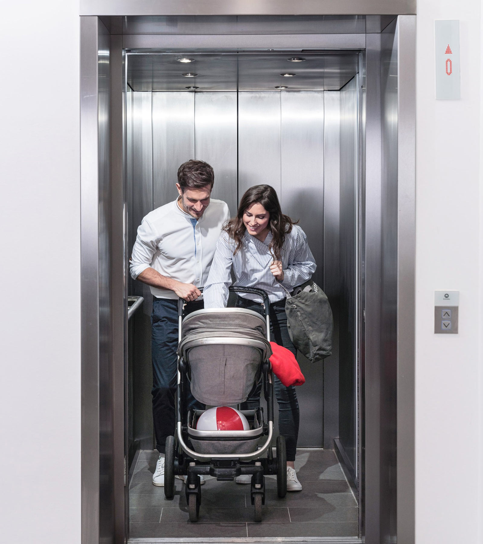 Mamma och pappa med bebis i barnvagn åker hiss tillsammans