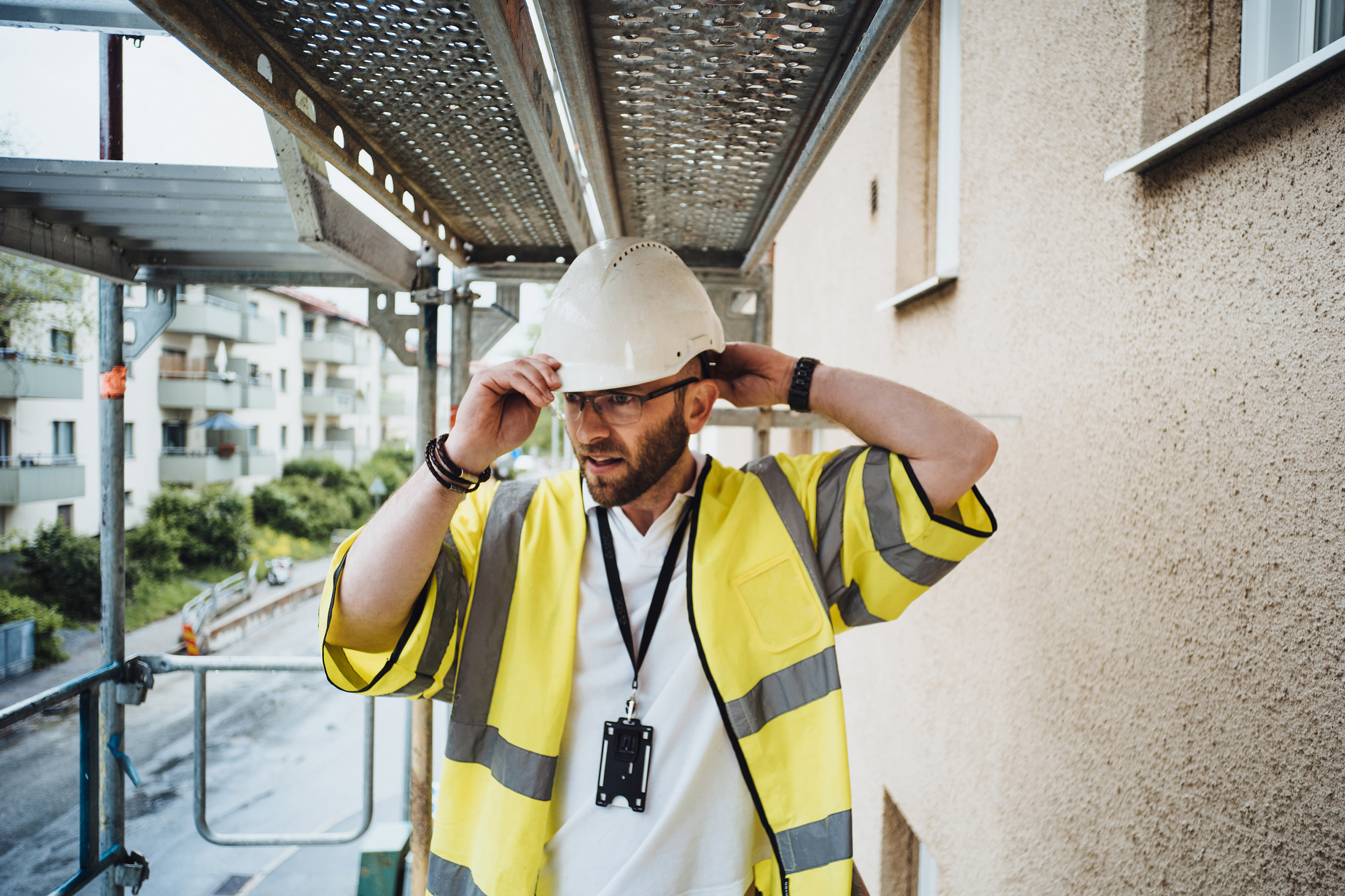 Manlig projektledare går i byggnadsställning och rättar till sin bygghjälm